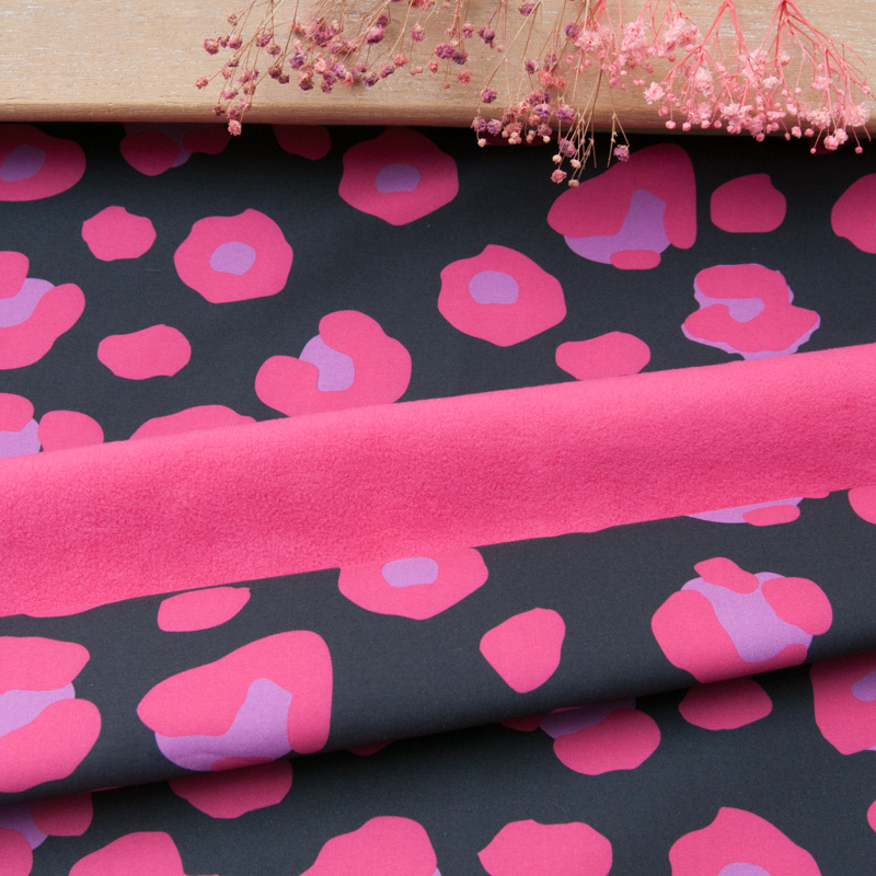 Softshell déperlant imprimé léopard fuchsia, roulé sur une planche en bois avec des fleurs séchées